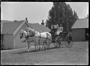 Two women and a baby seated alongside the driver of a two-horse buggy at Mendip Hills, Hurunui District.