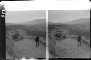 Unidentified man with camera and Model T Ford car overlooking a large mountain valley, unknown location