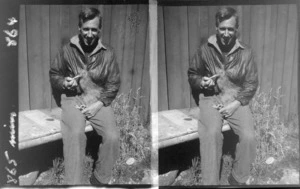 Unidentified man holding kiwi outside shed or hut, unknown location