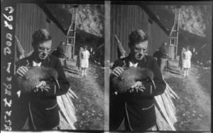 Unidentified man holding kiwi outside a shed or hut, unknown location