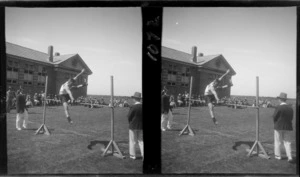 Community Sports Day, view of [Edgar Richard Williams?] attempting the high-jump in front of a large brick building with a crowd looking on at an unknown field location