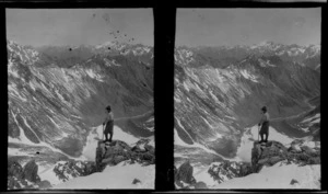 Unidentified mountaineer smoking a pipe on a rock edge, looking at the mountains opposite, West Coast region