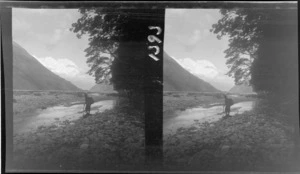 [Darran Mountains?], an unidentified man with an ice axe and pack beside the [Hollyford?] River and Valley, Fiordland National Park, Southland Region