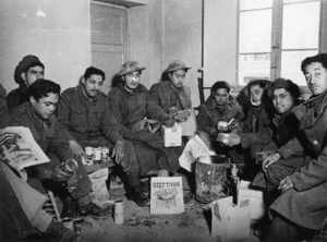 Kaye, George 1914- : Maori Battalion members unwrapping their Christmas patriotic parcels in a forward area, Faenza, Italy