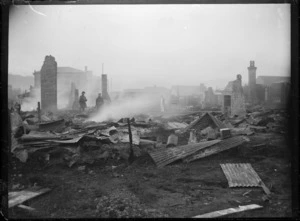 Houses destroyed by fire in Petone, with corrugated iron lying on the ground, several chimneys standing, and with the fire still smoking.