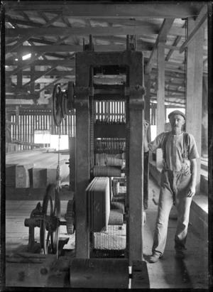 Worker standing beside machinery for cutting boards in a timber mill