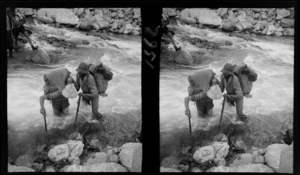 Unidentified men with packs crossing river, [Fiordland National Park, Southland Region]