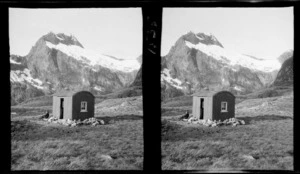 Unidentified man sitting outside alpine hut, McKinnon Pass, Fiordland National Park