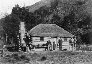 Unidentified men outside a thatched cottage in Halfway Bay, Otago