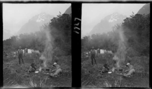 Three unidentified men resting beside a campfire with a tent pitched behind them and a mountain beyond, unknown location