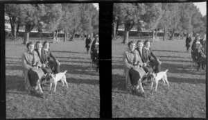 Portrait of two unidentified woman and a college girl with a dog sitting on a bench within Hagley Park, Christchurch City