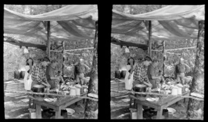 Edgar Wiliams on right with group of unidentified men, within a camp cooking area with table and tent fly, surrounded by bush at an unknown location, South Island