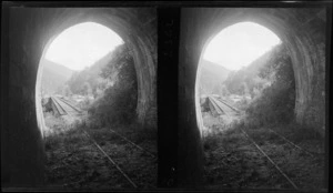 View out of a single line rail tunnel to a bridge and forested hills beyond at an unknown location, South Island