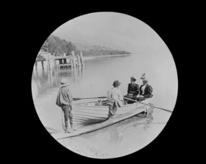 Unidentified people in row boat, including boy standing on plank, unidentified location