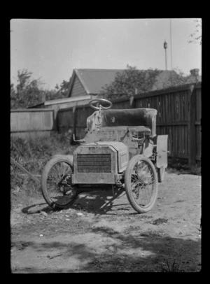 Near front view of a mud covered Ford Model [N?] car within an unknown backyard location, South Island