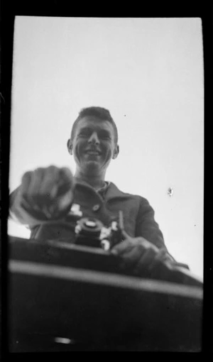 Portrait of an unidentified college boy on a stepladder holding a box brownie camera, [Dunedin City?]
