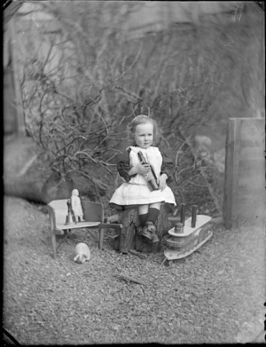 Edgar Richard Williams, sitting on a tree truck and playing with toys, location unidentified
