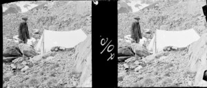 Unidentified man, near a pitched tent, on rocky mountains, location unidentified