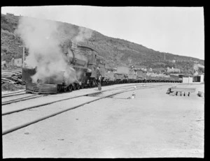An unidentified train driver with a steam train pulling timber loaded carriages at Kakahi Station, Manawatu-Whanganui Region