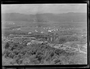 View over the settlement of Kakahi, with sawmill, stacked timber, rail yards and bridge and residential houses with forest covered hills beyond, Manawatu-Whanganui Region