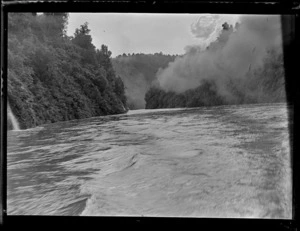 View off a boat on the Whanganui River with steep plant covered river banks and forest beyond