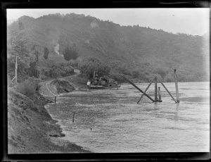 View of a path to houses above and several riverboats moored on the riverbank of the Whanganui River with forest covered hills beyond, Pipiriki