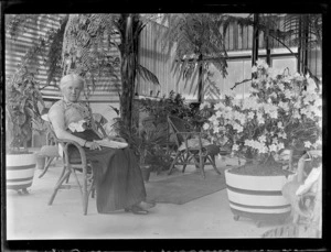 Lydia Williams sitting in a chair within a solarium of Pipiriki House with potted plant, Pipiriki, Whanganui River District