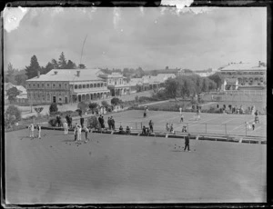 Unidentified men playing lawn bowls, men and women playing tennis, including Hot Springs Hotel and other stores to the left, Te Aroha, Waikato District