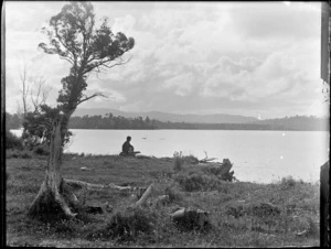 Edgar or Owen Williams sitting on a log looking out over a lake, Catlins District