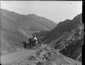 Unidentified men riding on horse and cart through mountain area, [Queenstown-Lakes District]