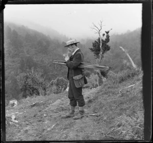 Unidentified man, propably William Williams, lighting up his pipe, with a camera stand under his arm and bag hanging off his shoulder, unidentified location