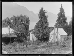 View of a cottage and two huts in front of trees above Lake Wakatipu with the Remarkable Mountain Range beyond, Queenstown, Central Otago Region