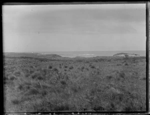 View of tussock covered dunes to an unknown bay with a lighthouse beyond, [Catlins District, South Dunedin, Otago Region?]