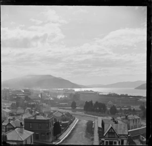 View of Dunedin City streets with the 'Howell & Co' building (foreground), the railway yards, (centre) and wharf area with docked sailing ships in Otago Harbour beyond