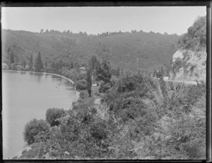 Scene, Rotorua, Bay of Plenty Region, showing a lake and a motocar on a road adjacent