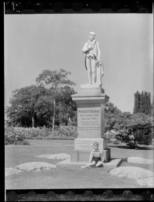 Unidentified boy sitting at the foot of the Robert Burns statue, Botanic Gardens, Timaru