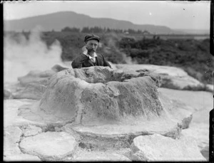 Unidentified man [William Williams?] sitting next to inactive cone geyser, Rotorua area, Bay of Plenty
