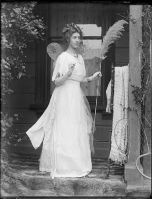 Unidentified young woman, dressed in a fairy costume, standing outside of house on porch, unknown location