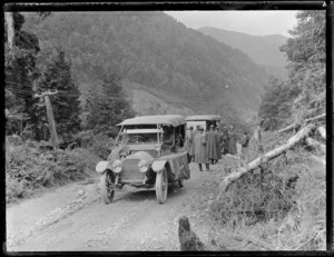 An unidentified group of people on an unknown hill shingle road with two Cadillac [Model 30?] Touring Cars with forest covered mountains beyond, [West Coast Region?]