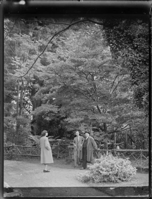 Two unidentified men and a woman on a walk track in front of a wooden fence and tall trees within [Hagley Park?], Christchurch City, Canterbury Region