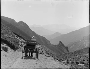 An unidentified person on a two horse drawn wagon on [Skippers Canyon Road?], Queenstown District with mountains beyond, Central Otago Region