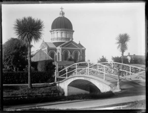 View of Otepuni Gardens with a stream, bridge and cabbage trees in front of Saint Marys Basilica on Tyne Street, Invercargill City, Southland Region