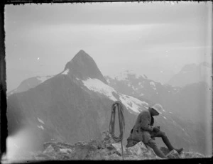 [Jack Murrell] sitting on Mount Wilmur with Mount Kepka in background, during Edgar Williams and Jack Murrell's climbing expedition in the Southern Alps, Fiordland National Park