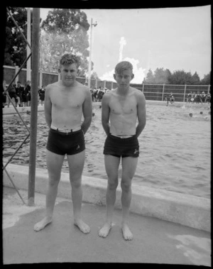 Two unidentified boys in togs with school children behind, at a public swimming pool