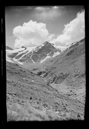 An unidentified man on the upper tussock covered Forbes River Valley below the South Forbes Glacier and The Onlooker peak, Inland Canterbury Region