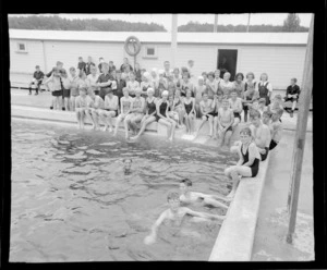 Group portrait of unidentified man with school children in togs at a public swimming pool