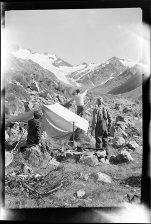 Two unidentified men and a woman making camp high in the Forbes River Valley, looking to Mount D'Archiac, the South Forbes Glacier and The Onlooker peak, Inland Canterbury Region