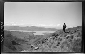 Landscape view, unidentified man on top of hill looking out towards hills, bay and mountain, Kaituna area, Banks Peninsula, Canterbury