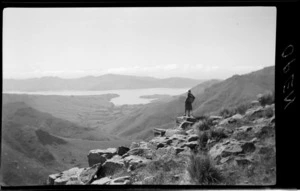Landscape view, unidentified woman on top of hill looking out towards hills, bay and mountain, Kaituna area, Banks Peninsula, Canterbury