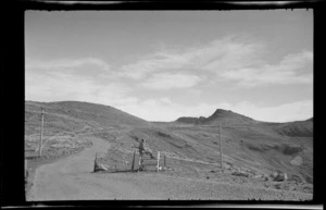 View of the Summit Road with Alice Williams sitting on a wooden stile with Castle Rock in the distance, Port Hills, Banks Peninsula, Canterbury Region